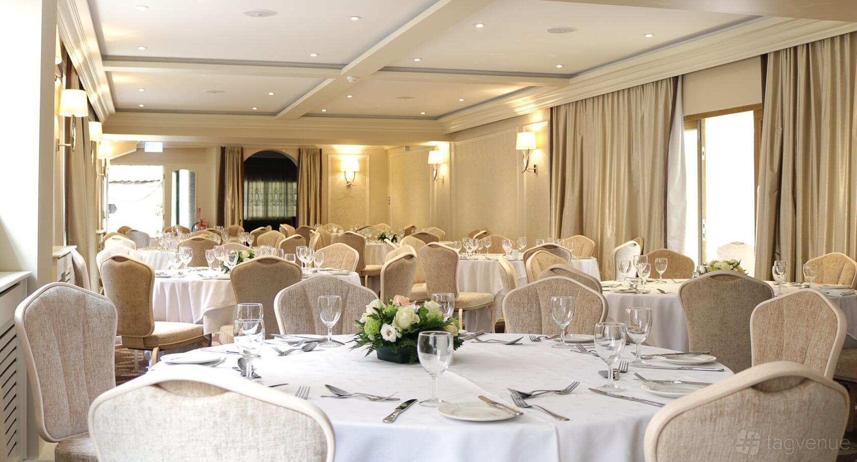 An event space with round tables covered in white linens, floral centerpieces, and upholstered chairs at Swan Hotel Wells.