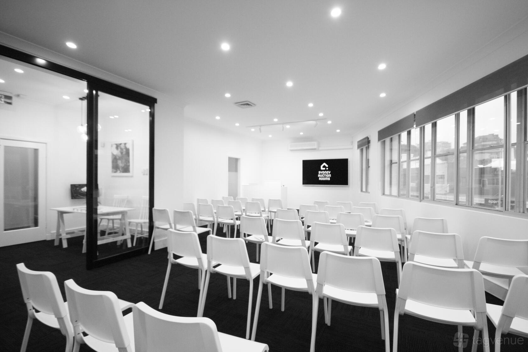 An auditorium with rows of white chairs, a projector screen, and large windows at Sydney Conference Venue.