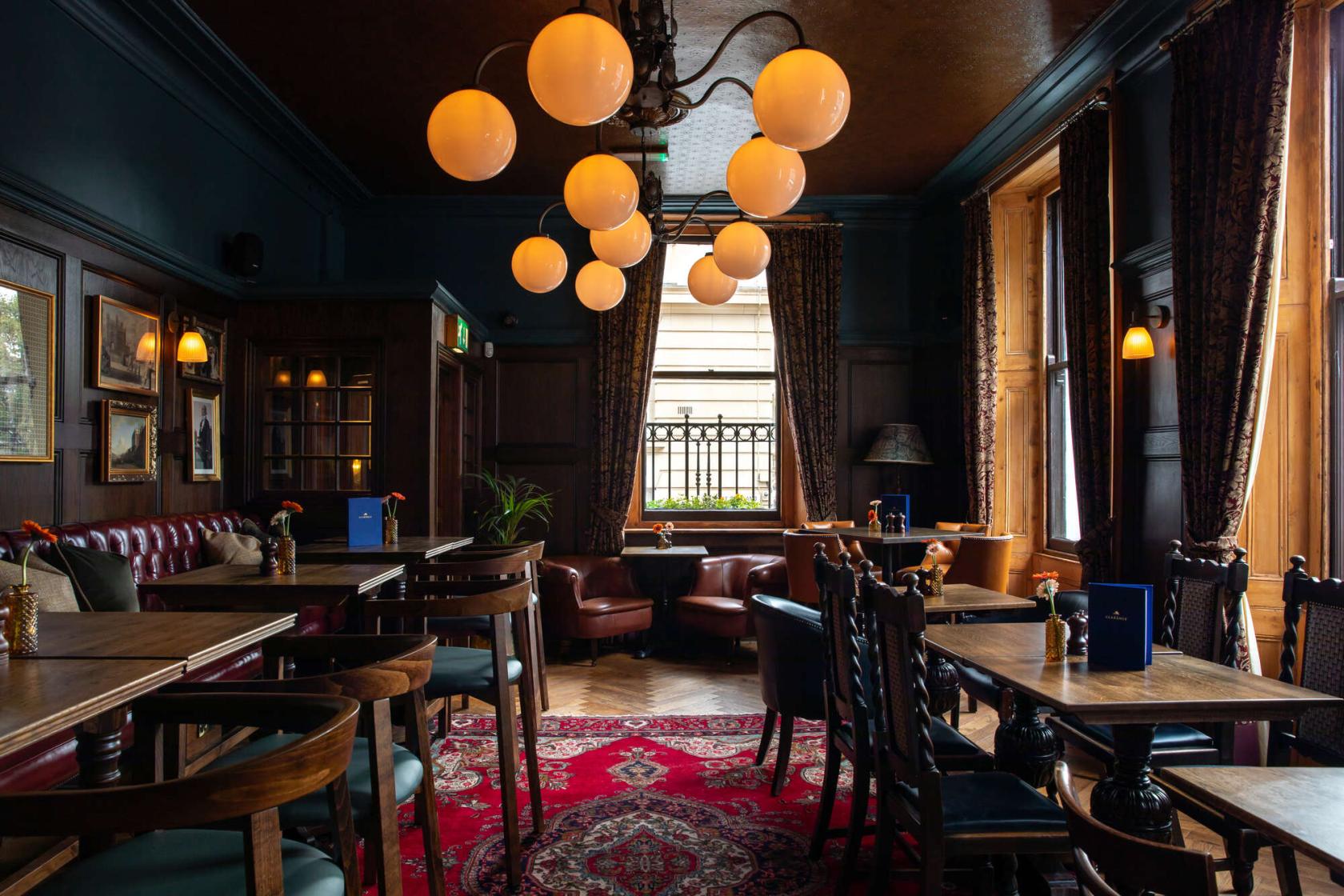 An event space in a pub with dark wood furnishings, leather seating, globe pendant lights, and carpeted floors at The Clarence Whitehall.
