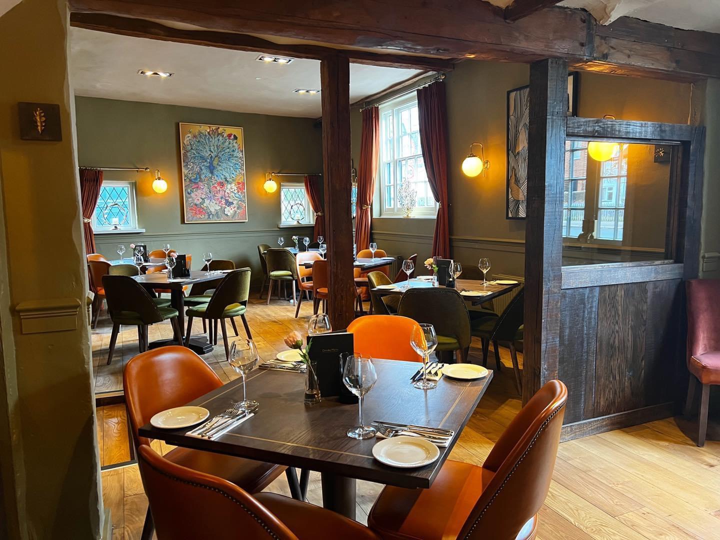 A pub dining room with wooden floors, large windows, orange chairs, and colorful artwork at The Flying Horse.