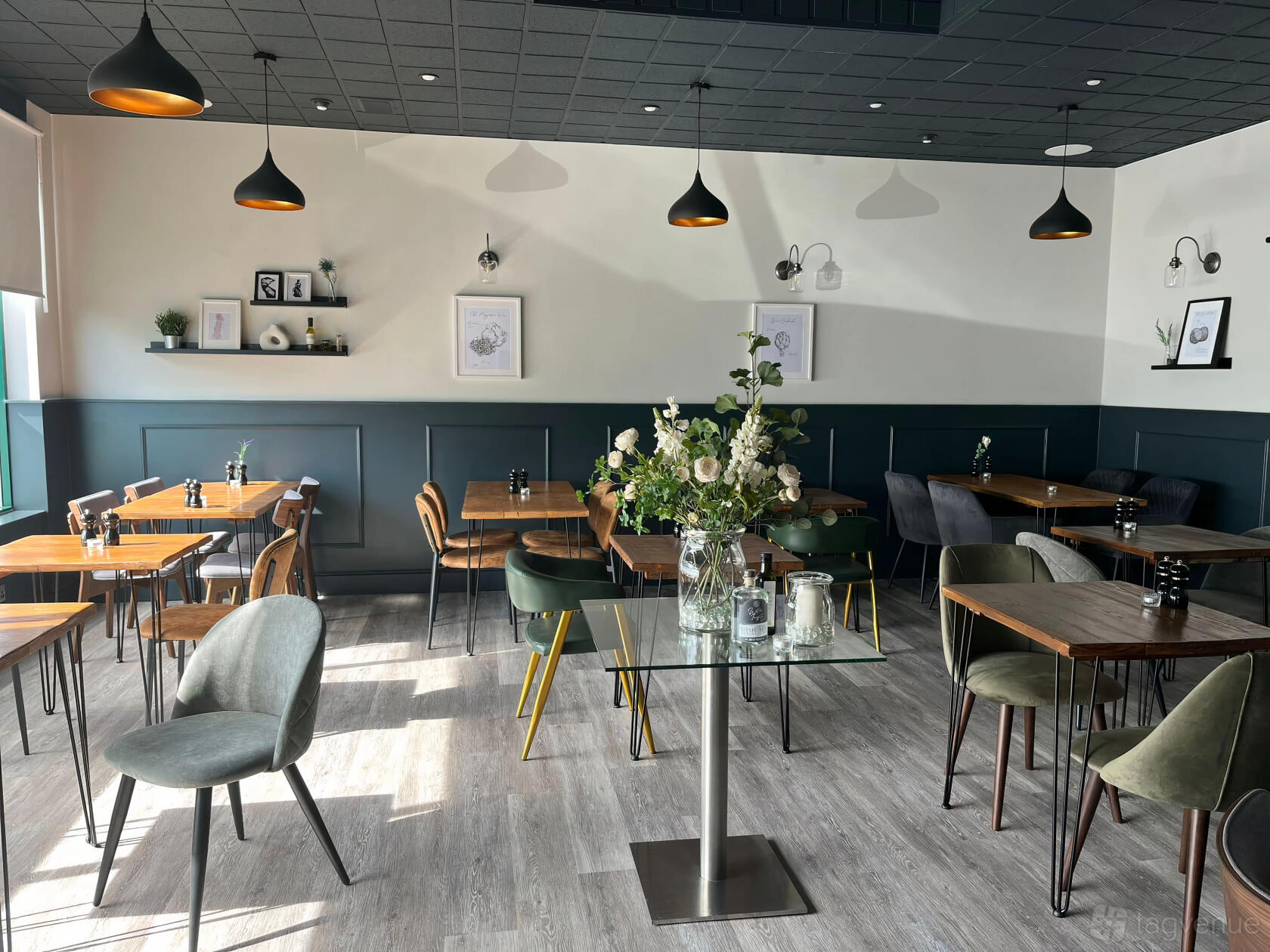 A restaurant with wooden tables, mixed velvet chairs, floral centerpieces, and framed wall art at White Truffle.