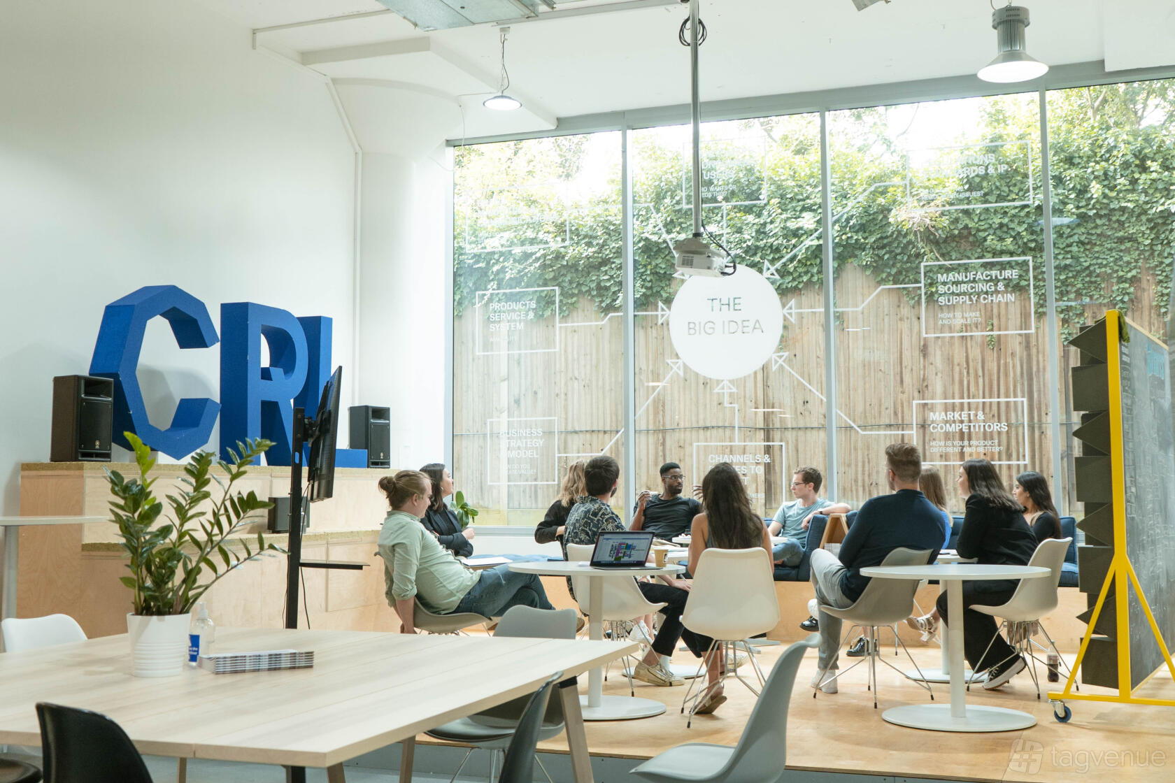 An event space with floor-to-ceiling windows, natural light, and round tables at Plus X Innovation Slough.