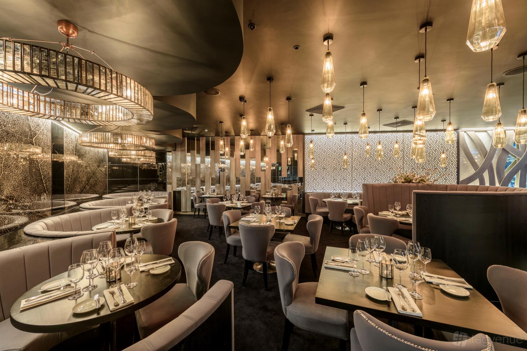 A restaurant with curved banquettes, upholstered chairs, mirrored walls, and pendant lighting at Gaucho Broadgate.