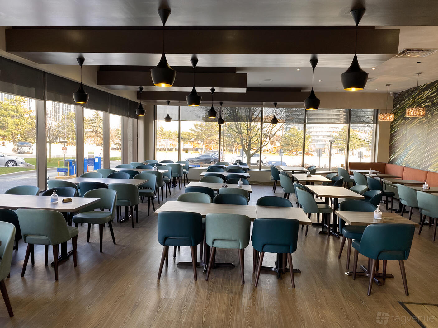 A restaurant with floor-to-ceiling windows, pendant lights, and teal upholstered chairs at Tamarind Modern Indian Bistro.