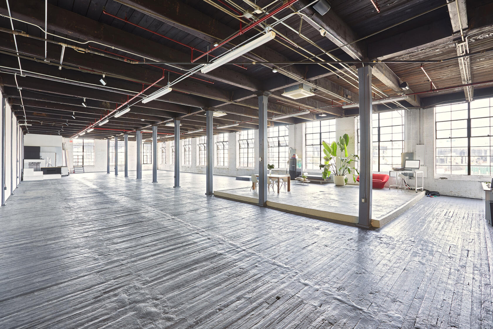 A photo studio with large industrial windows, exposed beams, and an open floor plan at Please Space Studios.