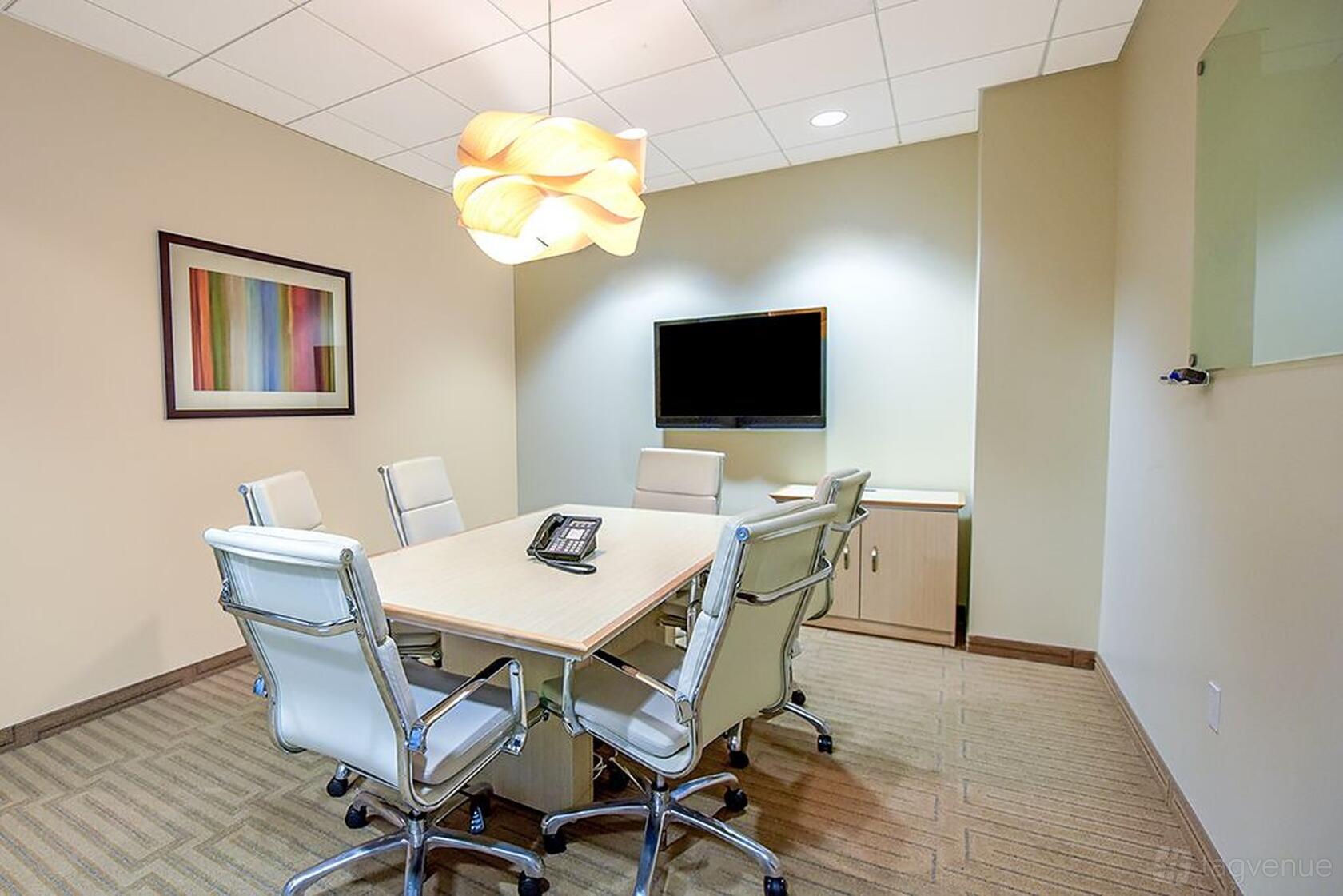 A coworking space with a rectangular conference table, six leather chairs, wall art, and a pendant light at Premier Workspaces - 4000 MacArthur Boulevard.