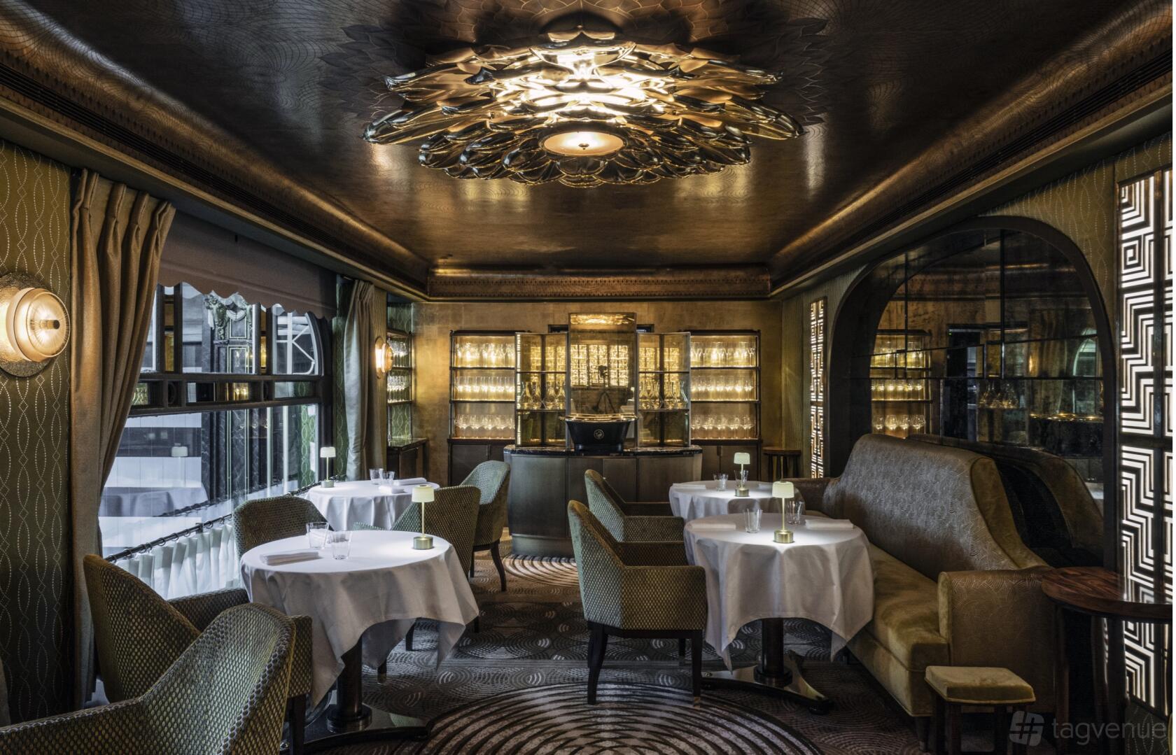 A hotel restaurant with round tables covered in white linens, plush chairs, and an ornate ceiling at 1890 by Gordon Ramsay.