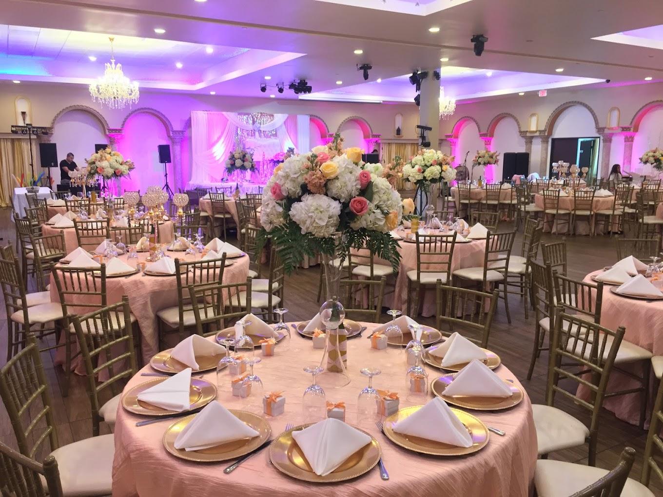 A banquet hall with round tables covered in pink linens, floral centerpieces, and chandeliers at Royal Banquet Hall & Conference Center.