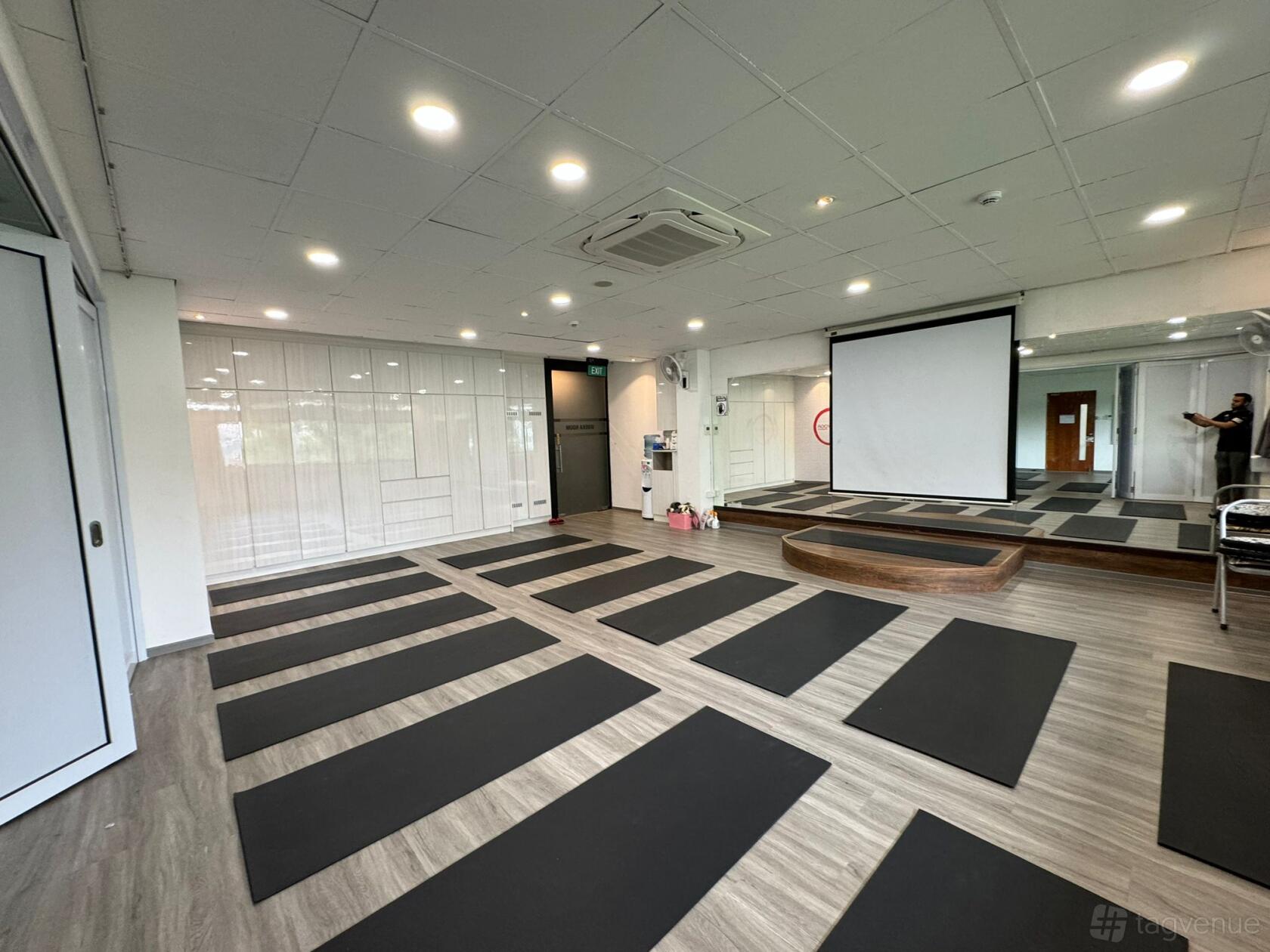 A yoga studio with black mats arranged on wood floors, wall mirrors, and a projector screen at Vyasa Yoga Singapore.