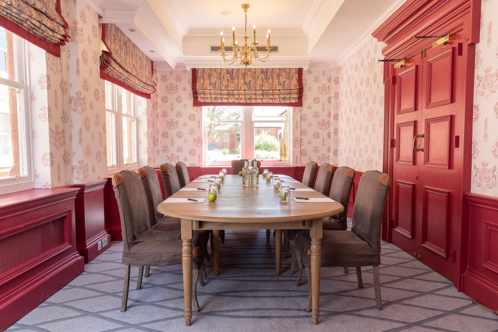 A meeting room with a long wooden table, brown upholstered chairs, patterned wallpaper, and chandelier at Pendley Manor Hotel.