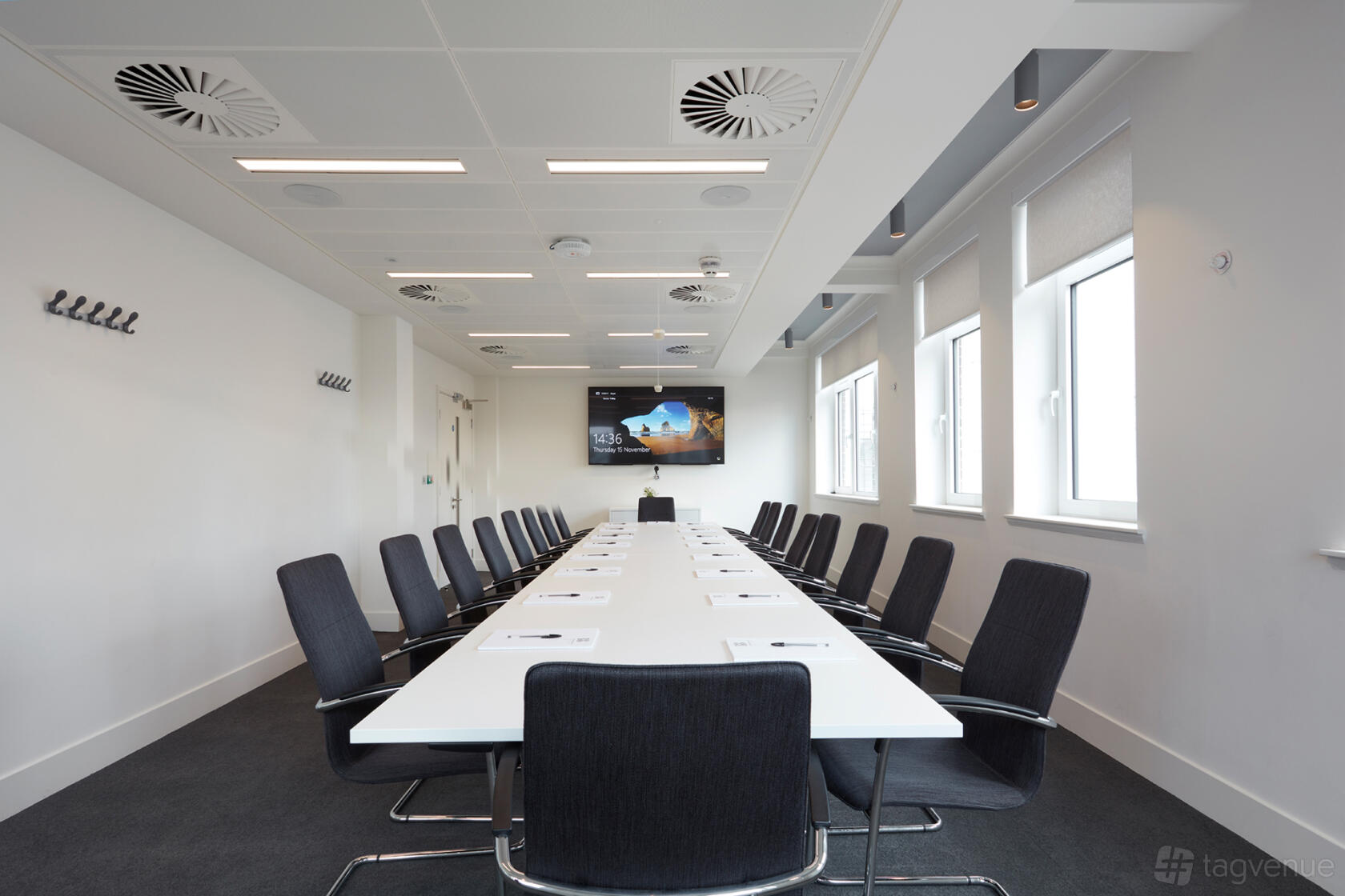 A meeting room with a long white conference table, black chairs, wall-mounted screen, and large windows at 18 Smith Square.
