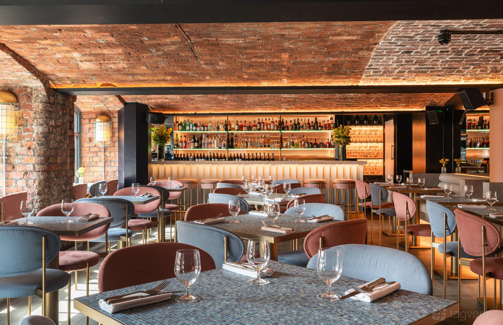 A restaurant with arched brick ceilings, contemporary seating, and a backlit bar at MAYA Manchester.