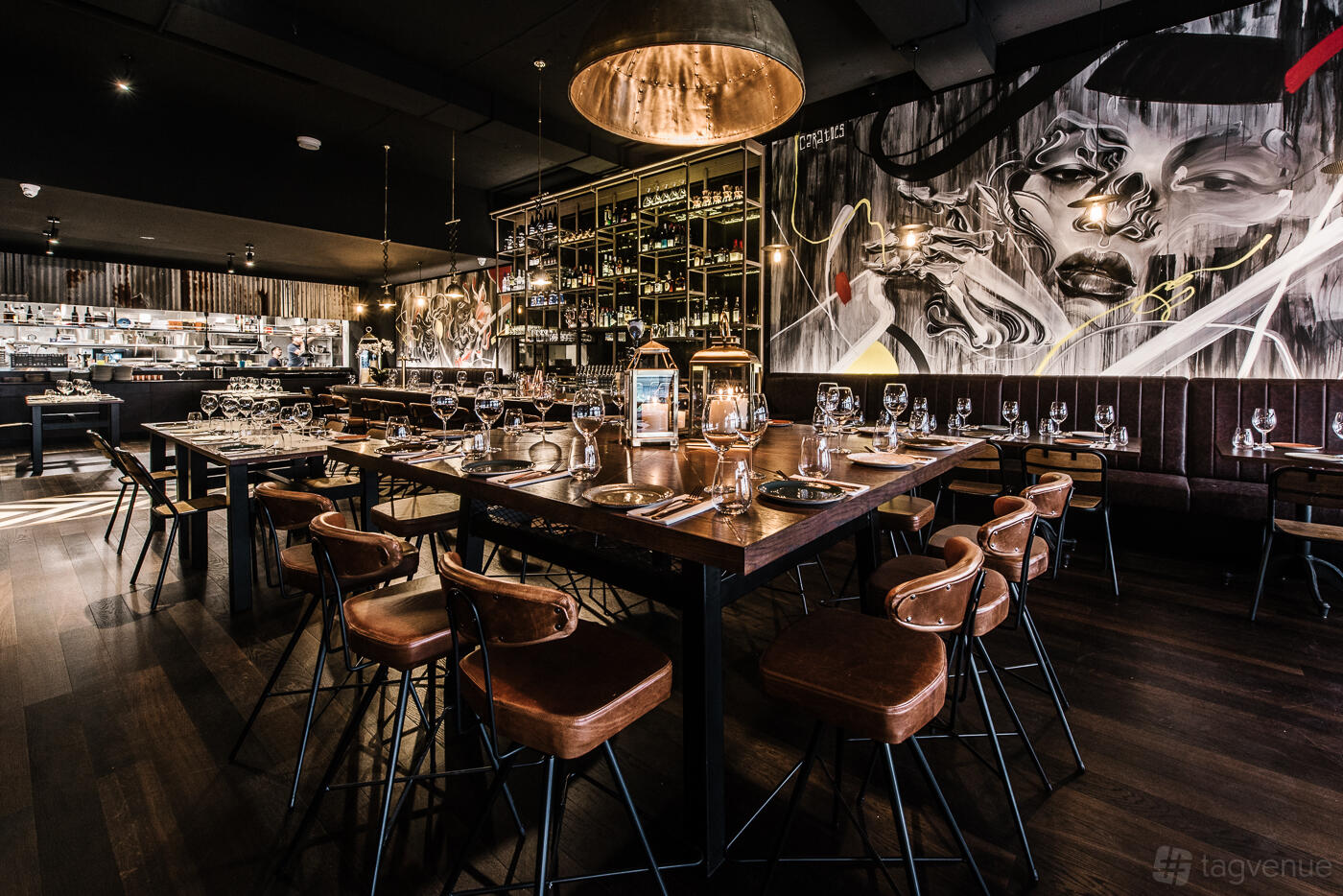 A restaurant with high tables, leather stools, a mural wall, and a wine rack at Eastside Bar and Grill.