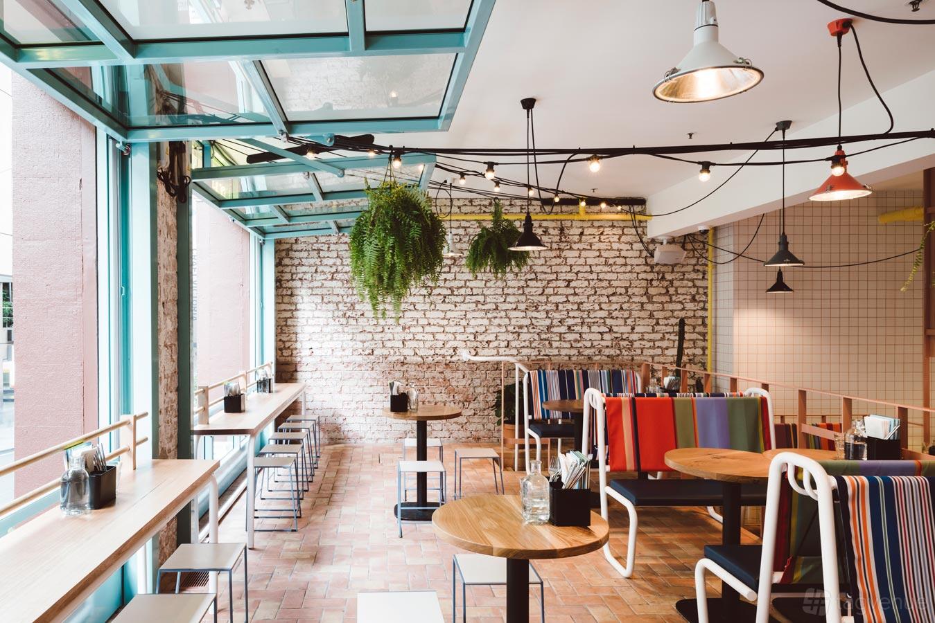 An event space with exposed brick walls, large windows, hanging plants, and striped banquette seating at Fonda Mexican @ Flinders Lane.