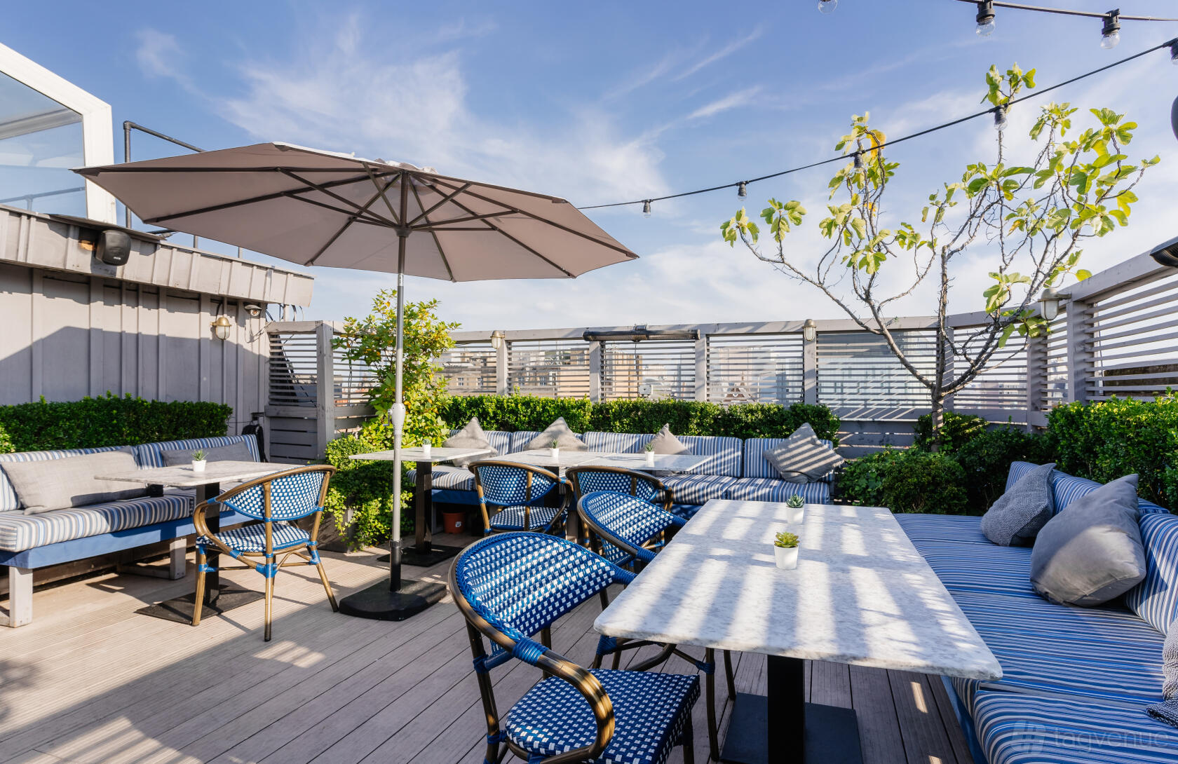 A terrace bar with marble tables, blue-striped bench seating, and a large umbrella at Century Club.