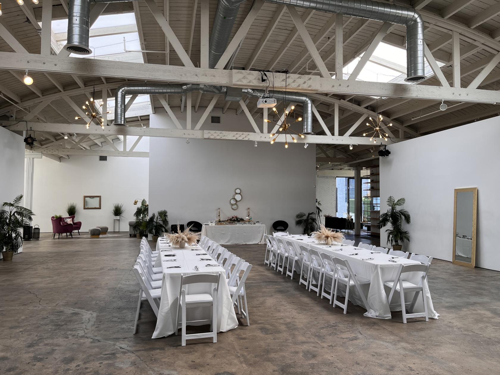 An event venue with skylights, exposed beams, and banquet tables with white chairs on the Main Floor at The East Angel.