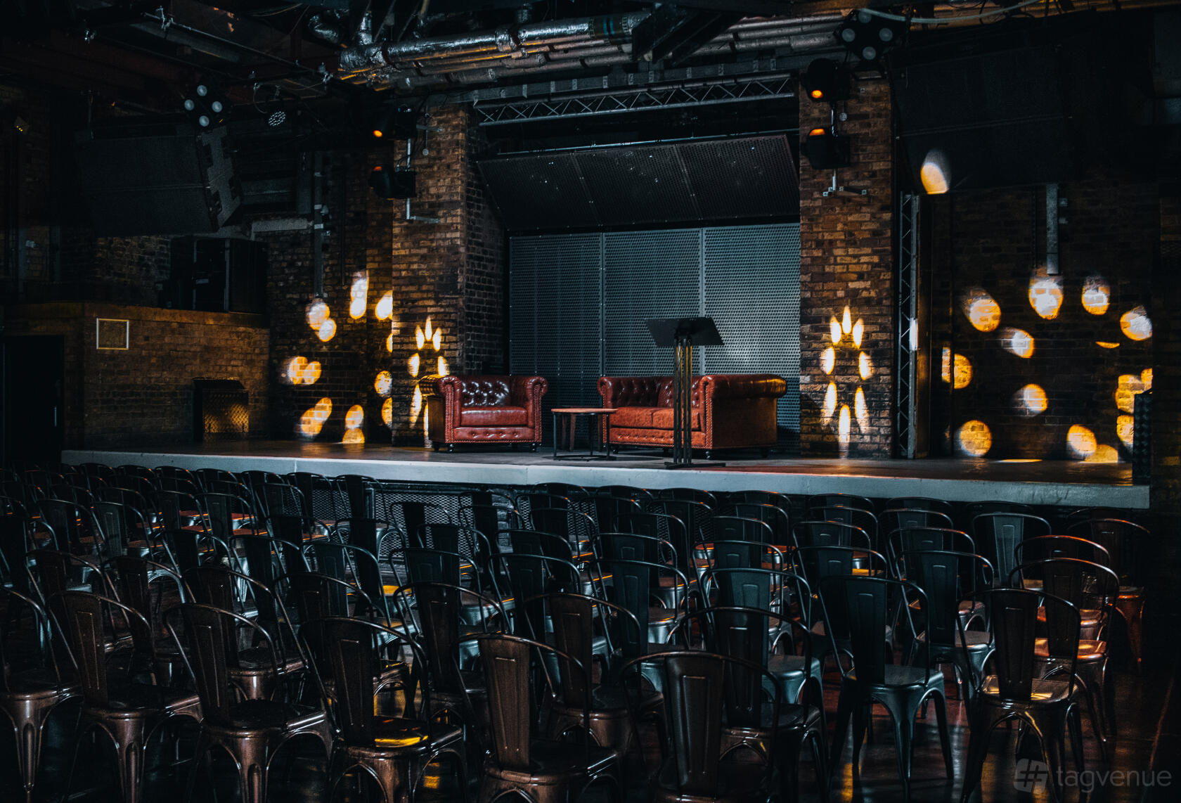 An event venue with a stage, exposed brick walls, theater seating, and leather sofas at fabric industrial arts events venue.