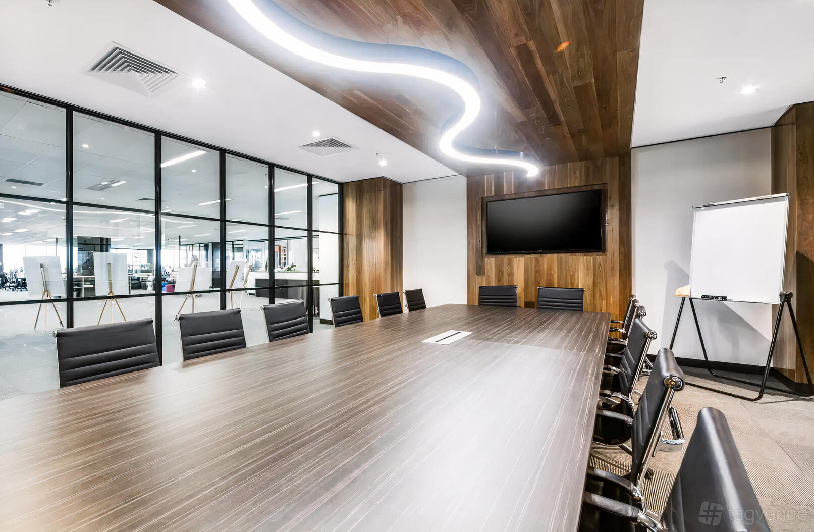 A boardroom with a long wooden table, black chairs, wall-mounted screen, and glass partitions at Waterman at Narre Warren.