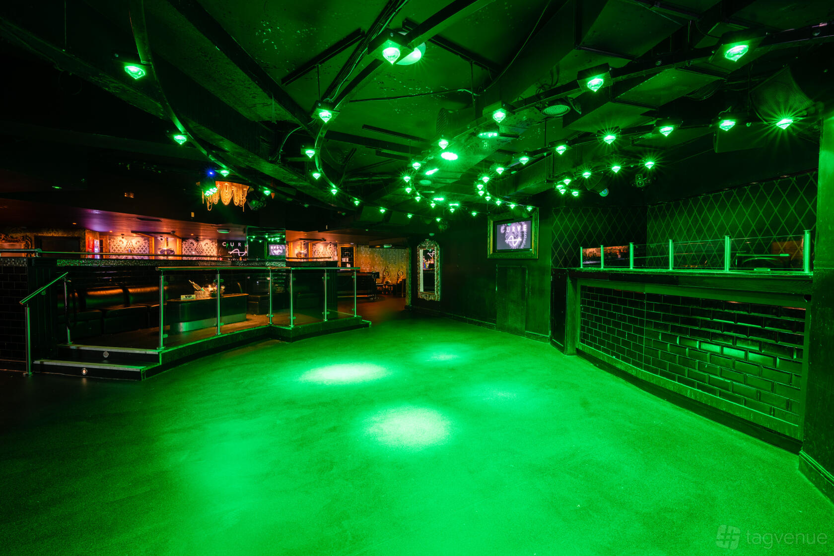 A nightclub event space with green ceiling lights, black brick walls, and a raised seating area at PRYZM Brighton.