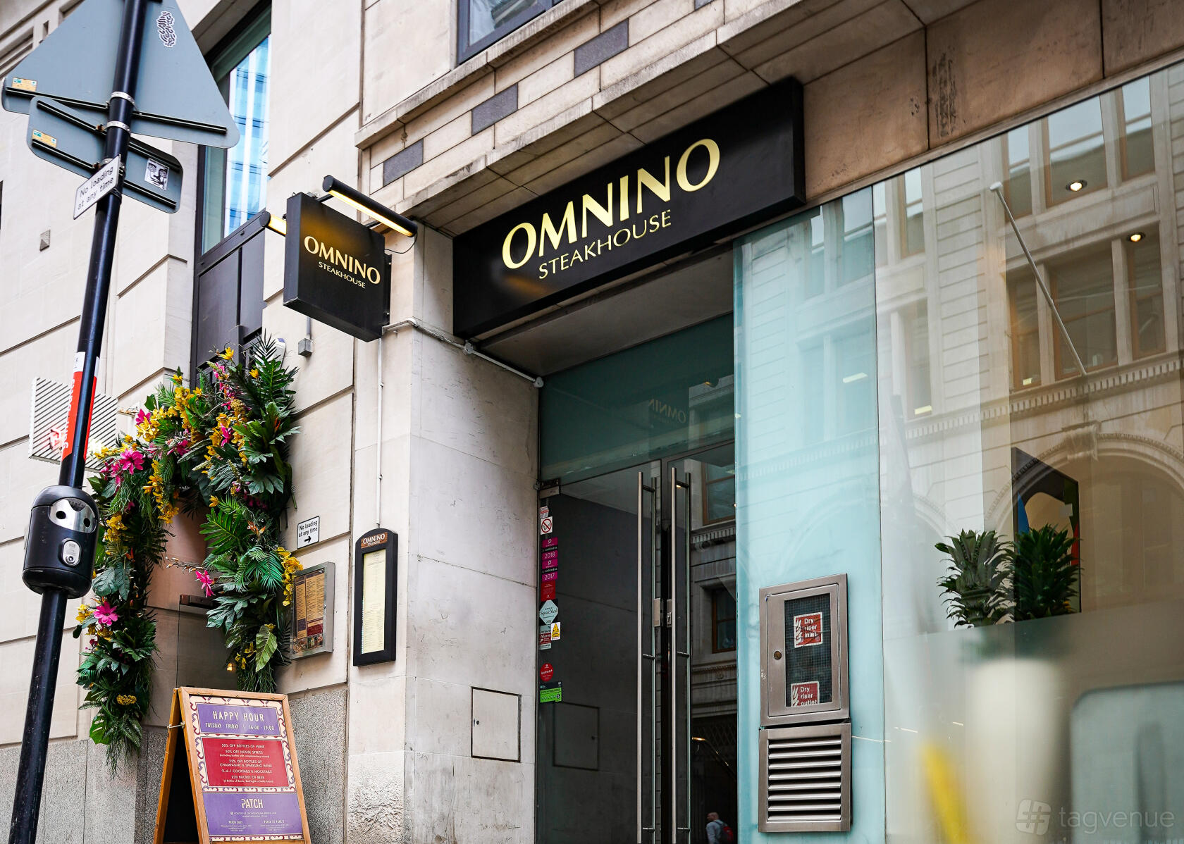A restaurant entrance with glass doors, floral decorations, and Omnino Steakhouse signage.
