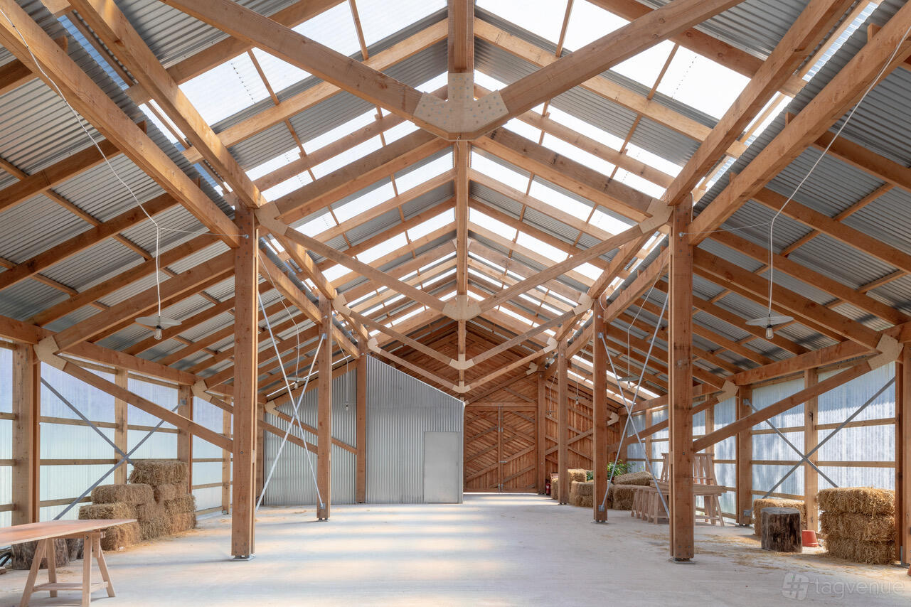 A barn with exposed wooden beams, corrugated metal roof, hay bales, and natural light at Oasis Farm Waterloo.
