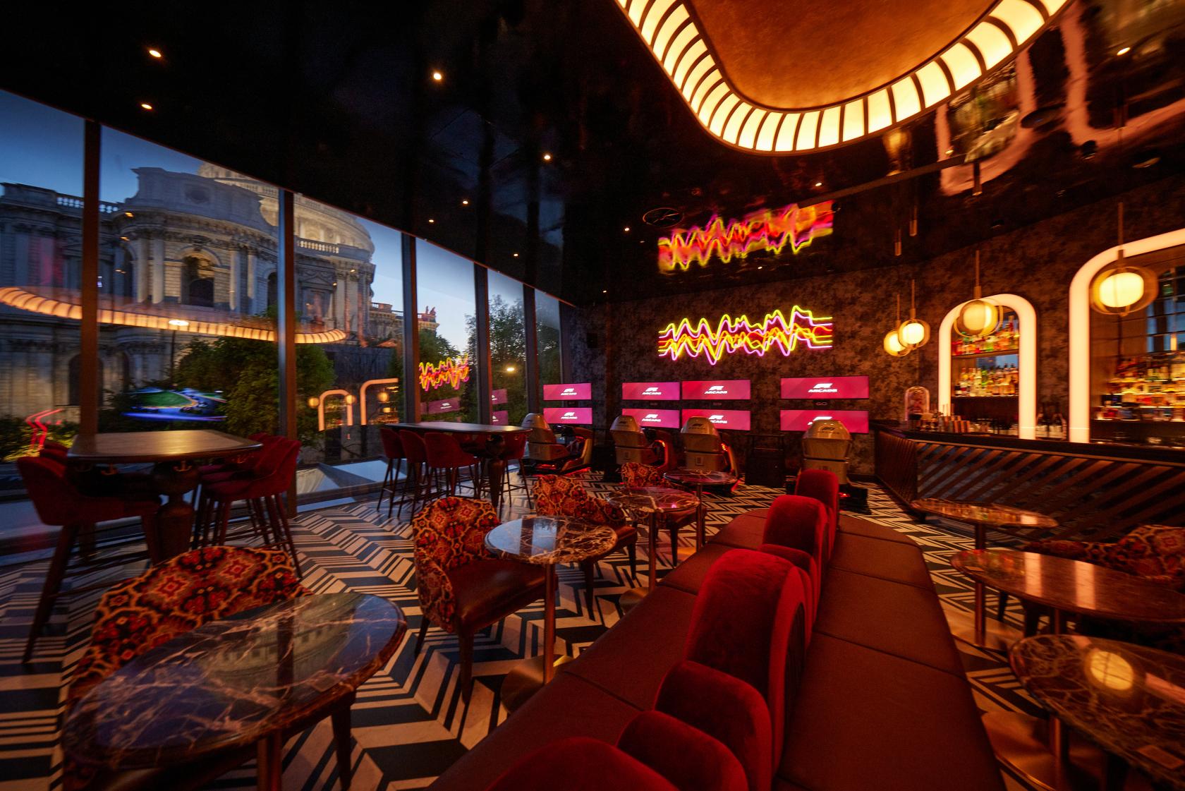 A cocktail bar with floor-to-ceiling windows, geometric floors, plush seating, and gaming screens at F1 Arcade, St Pauls, London.