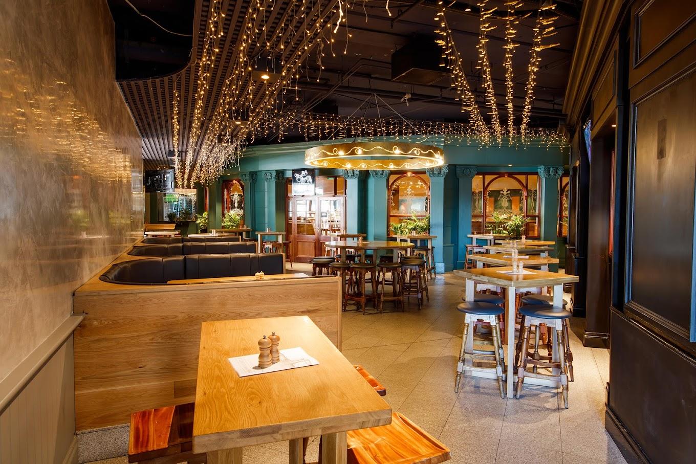 An event space in a bar with wood tables, booth seating, and string lights at Pig ‘N’ Whistle - Indooroopilly.