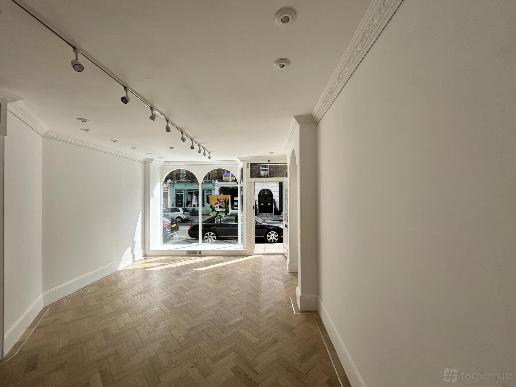 An art gallery event space with herringbone wood floors, white walls, and large arched windows at Casild Art.