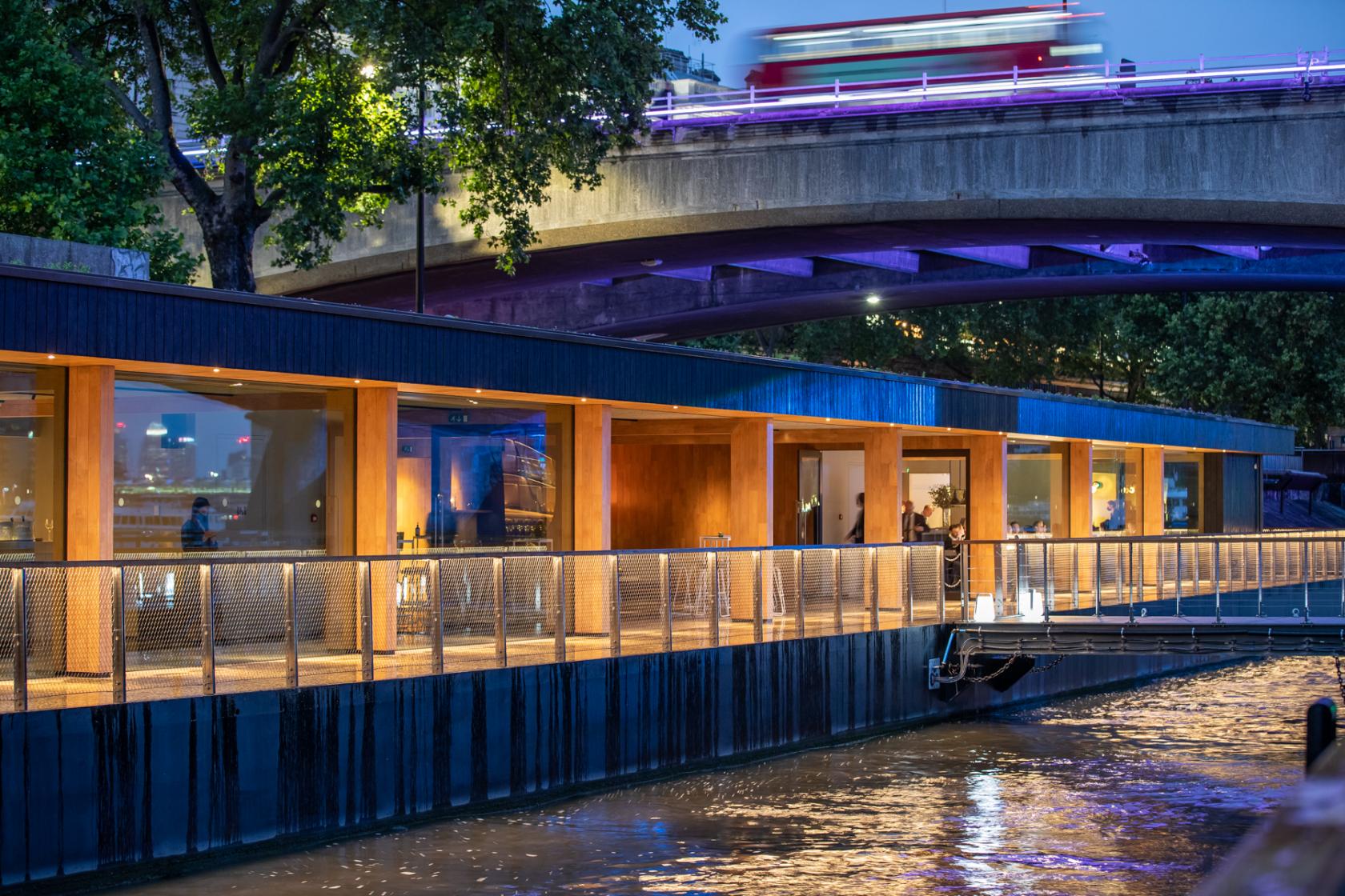 A boat venue with glass walls, warm lighting, and a waterside deck at Woods Silver Fleet.