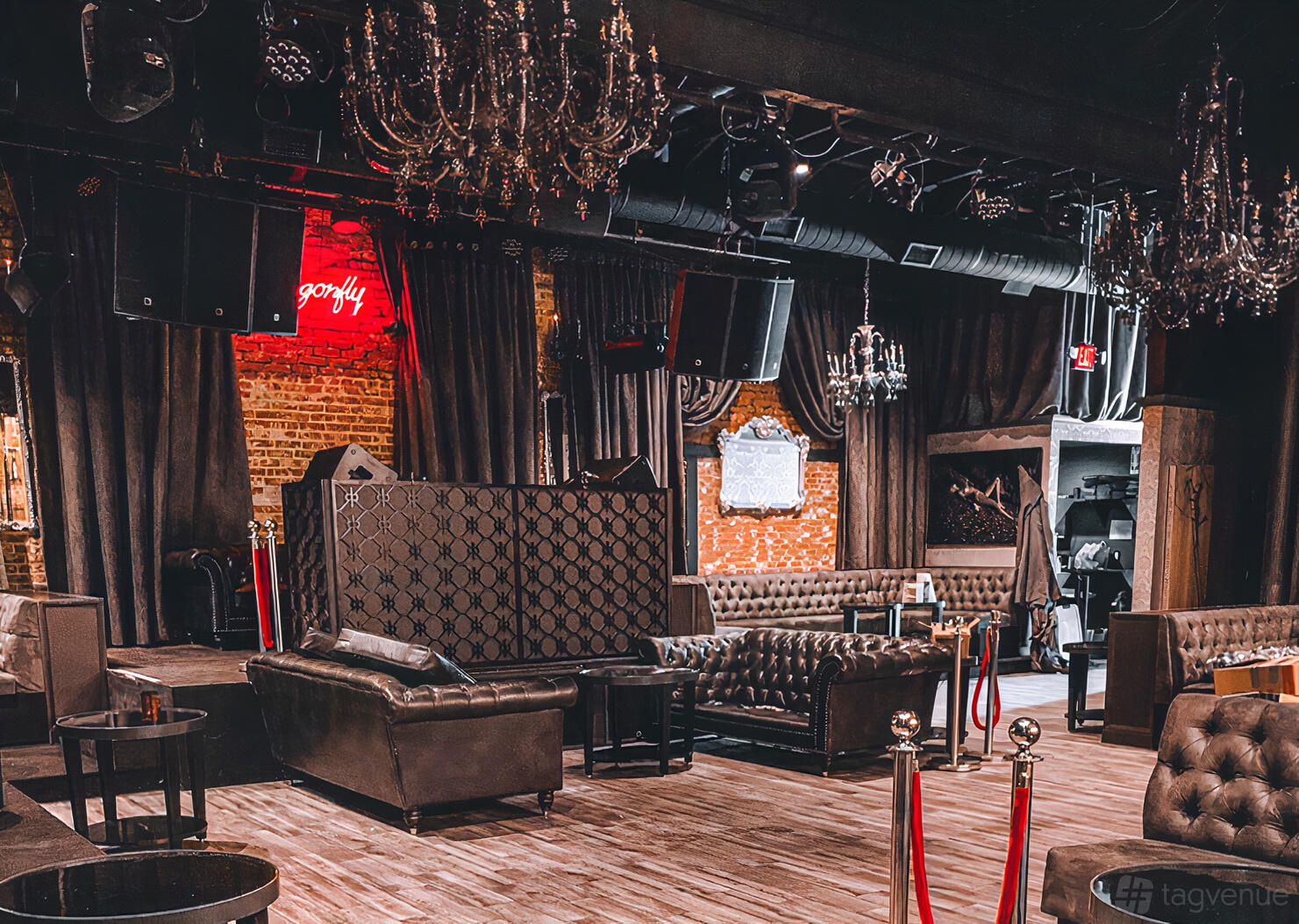 A nightclub with exposed brick walls, dark tufted leather sofas, chandeliers, and a neon sign at DRAGONFLY HOLLYWOOD.