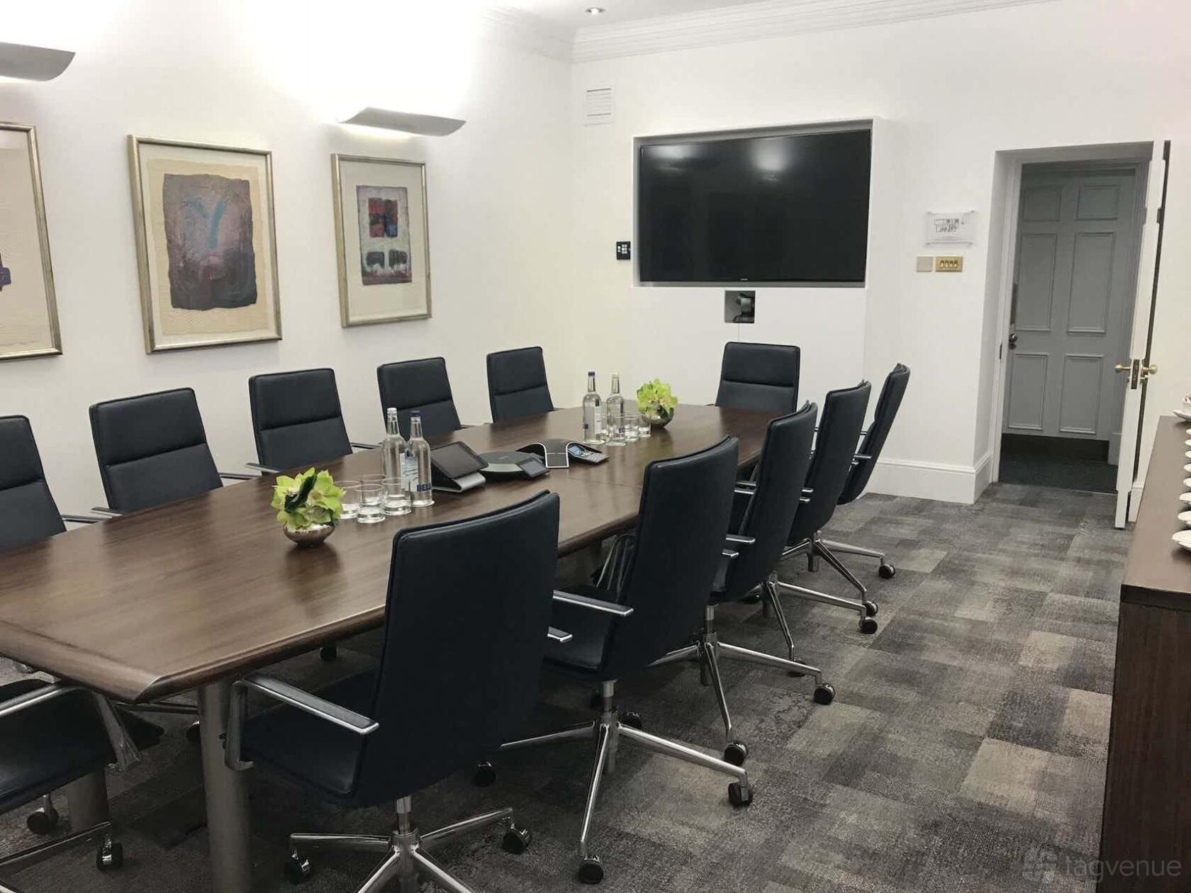 A meeting room with a long wooden table, black swivel chairs, wall art, and a large screen at 17 Cavendish Square.