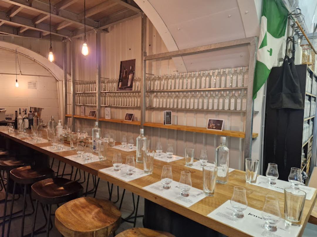 A bar with long wooden tables, tasting glasses, and shelves lined with bottles at Bermondsey Distillery.
