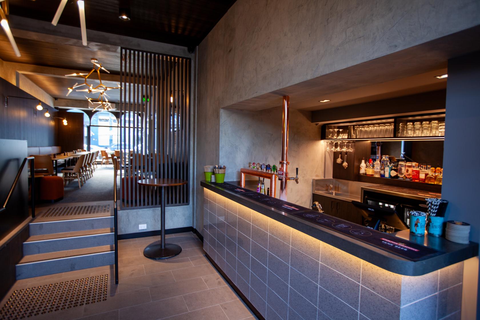 A dining room in a pub with a tiled bar, modern pendant lighting, and wooden slat dividers at Mt View Hotel.
