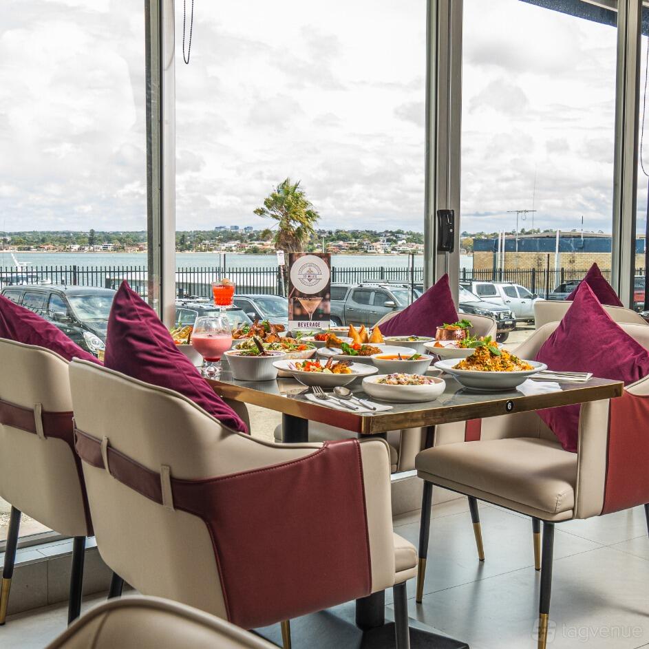 An event space with large windows, tan chairs, and a table set with Indian dishes at 32 Miles Indian Restaurant.