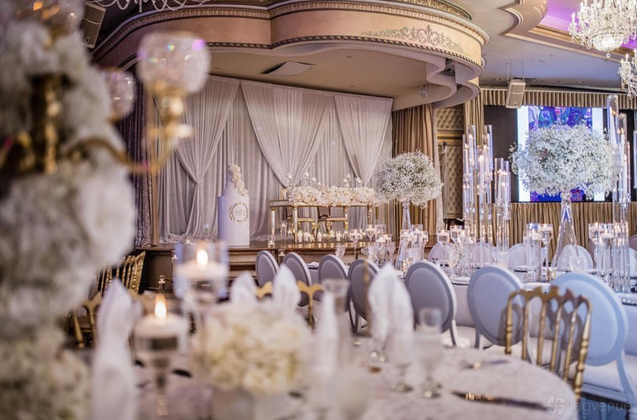 A ballroom with draped stage, gold chairs, floral centerpieces, and candlelit round tables at Da Mikelle Palazzo.