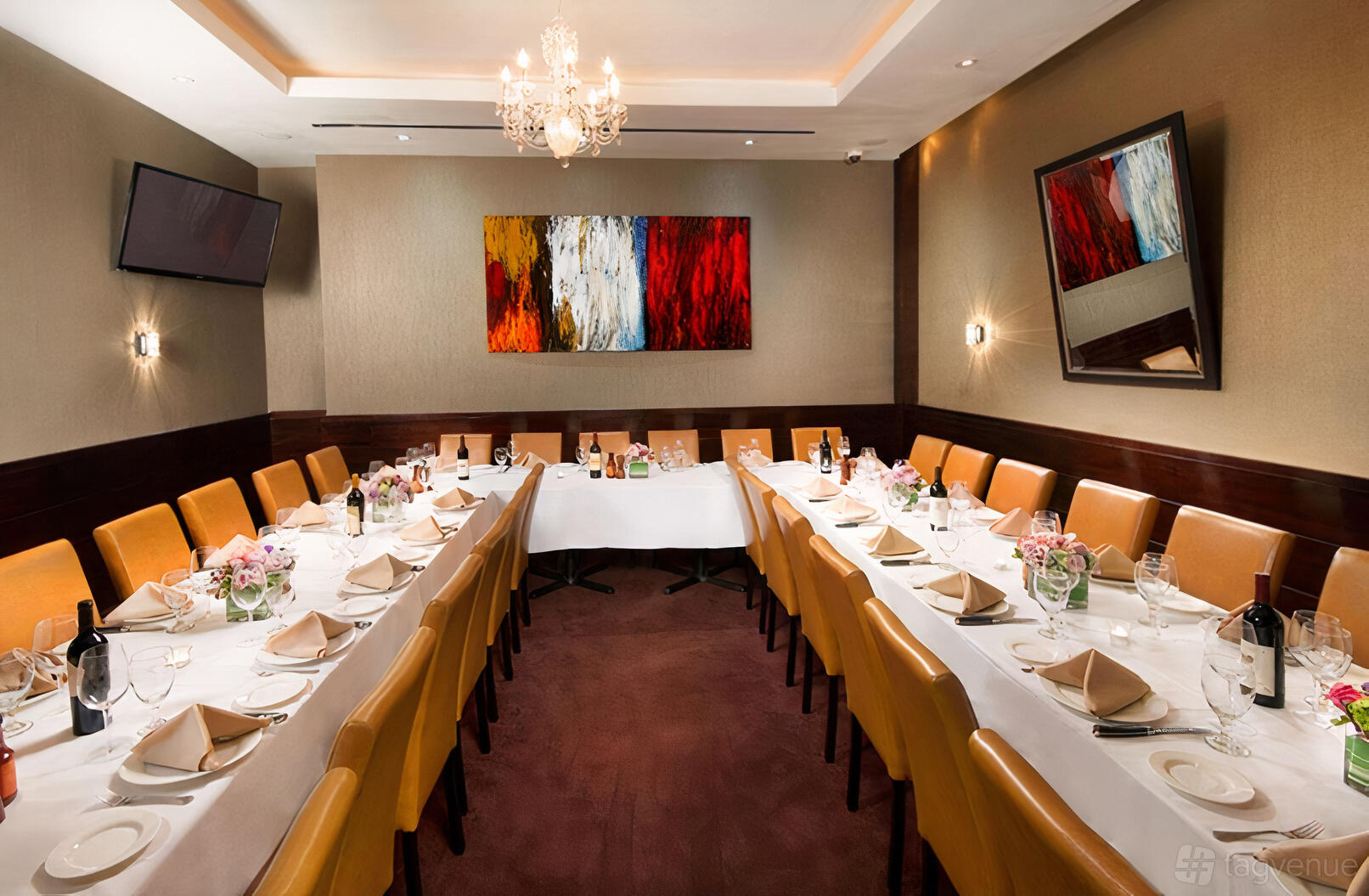 A private dining room with two long tables, leather chairs, chandeliers, and modern art at Empire Steak House West.