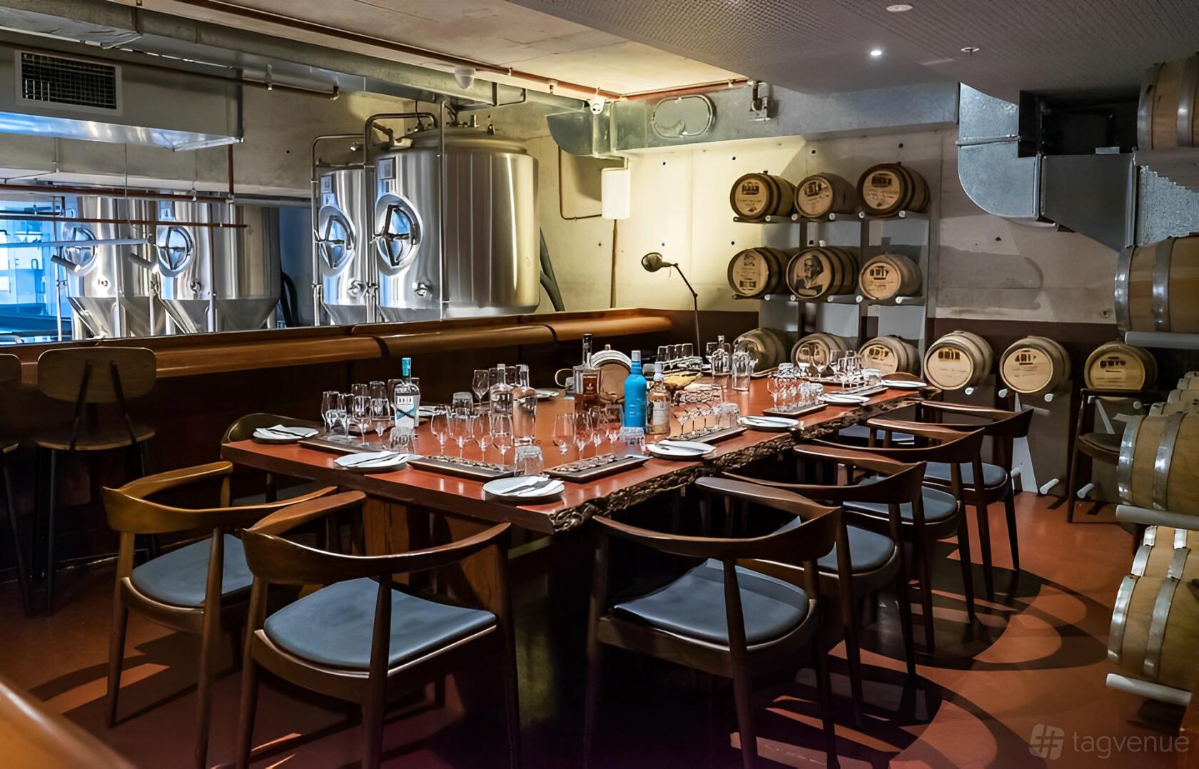 An event space with a long wooden table set for dining, surrounded by barrels and metal tanks at Brix Distillery.