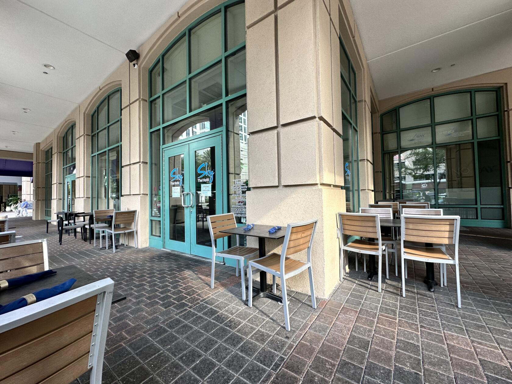 An outdoor restaurant patio with wood and metal tables and large arched windows at Sky Thai Sushi.