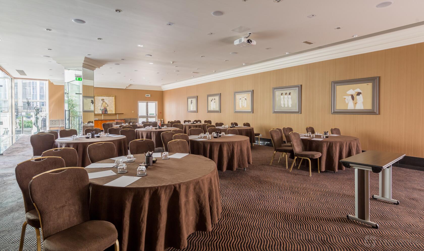 A meeting room with round tables covered in brown linens, chairs, and framed artwork at Radisson Blu Hotel, London Heathrow.
