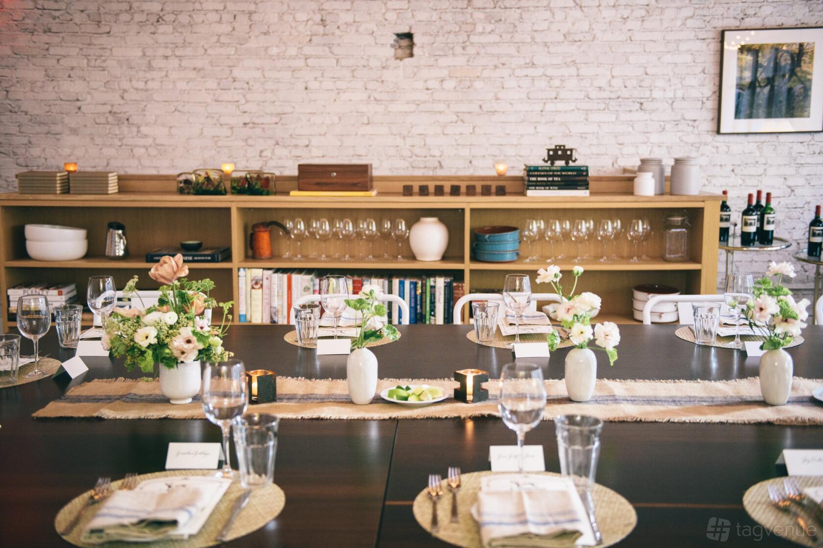 A kitchen venue with set dining tables, floral centerpieces, and a white brick wall at MM Kitchen Studio.
