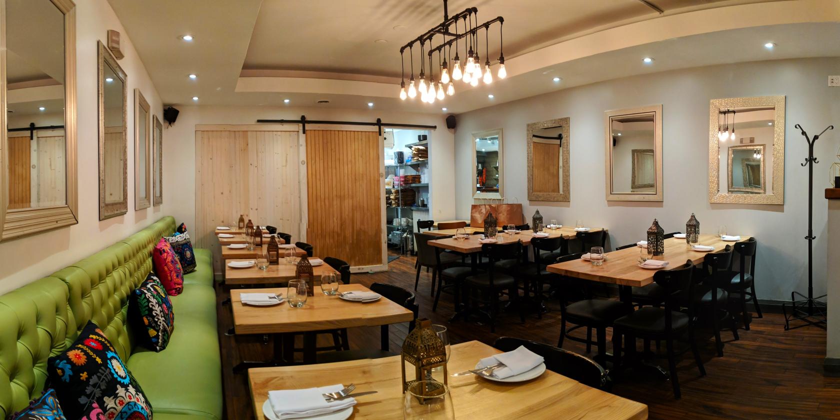 An event space with wooden tables, green upholstered bench seating, pendant lights, and decorative lanterns at Cumin Kitchen.