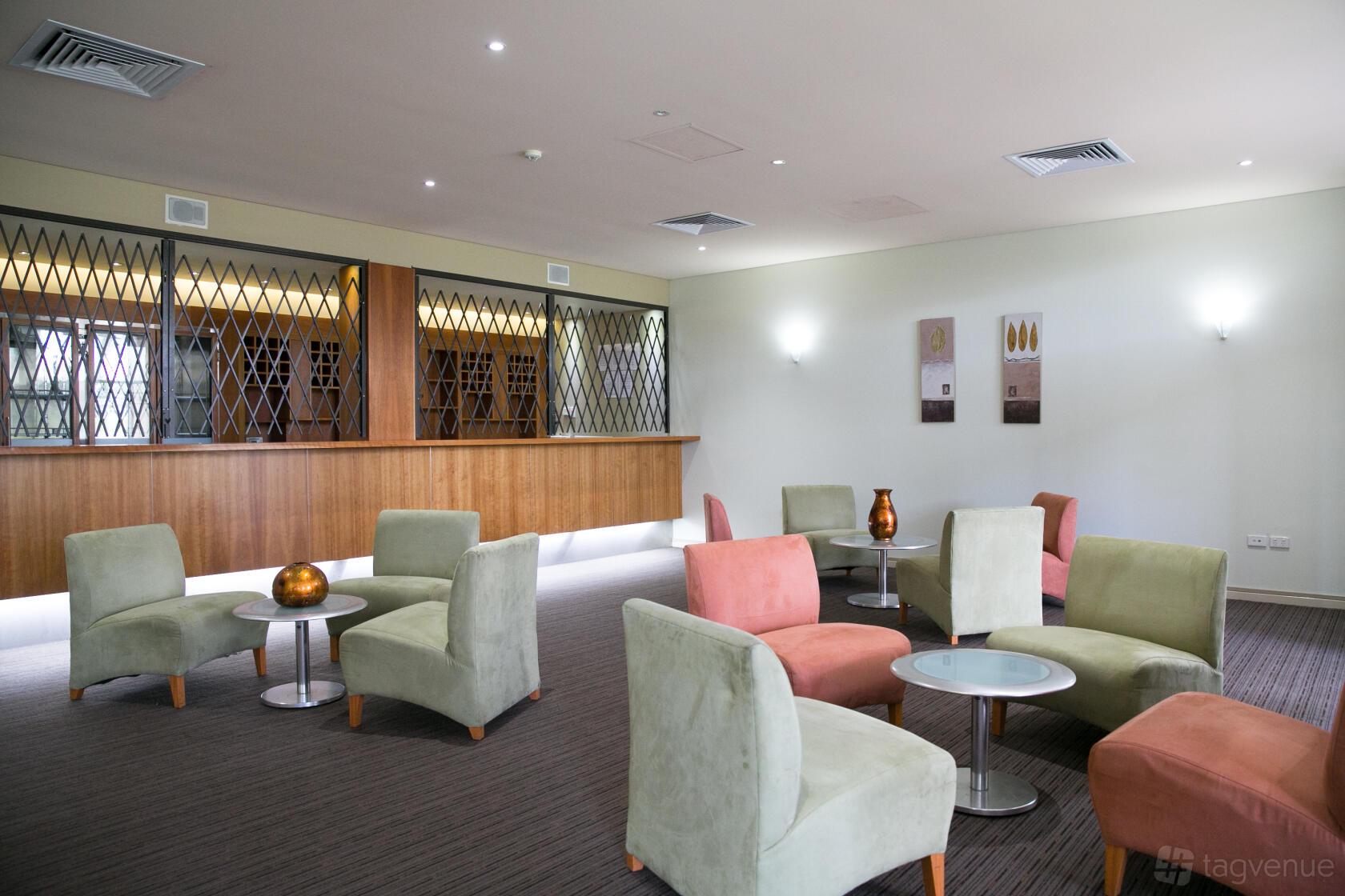 An apartment lounge with pastel armchairs, round tables, and a built-in wooden bar at Nesuto Mounts Bay Perth Apartment Hotel.