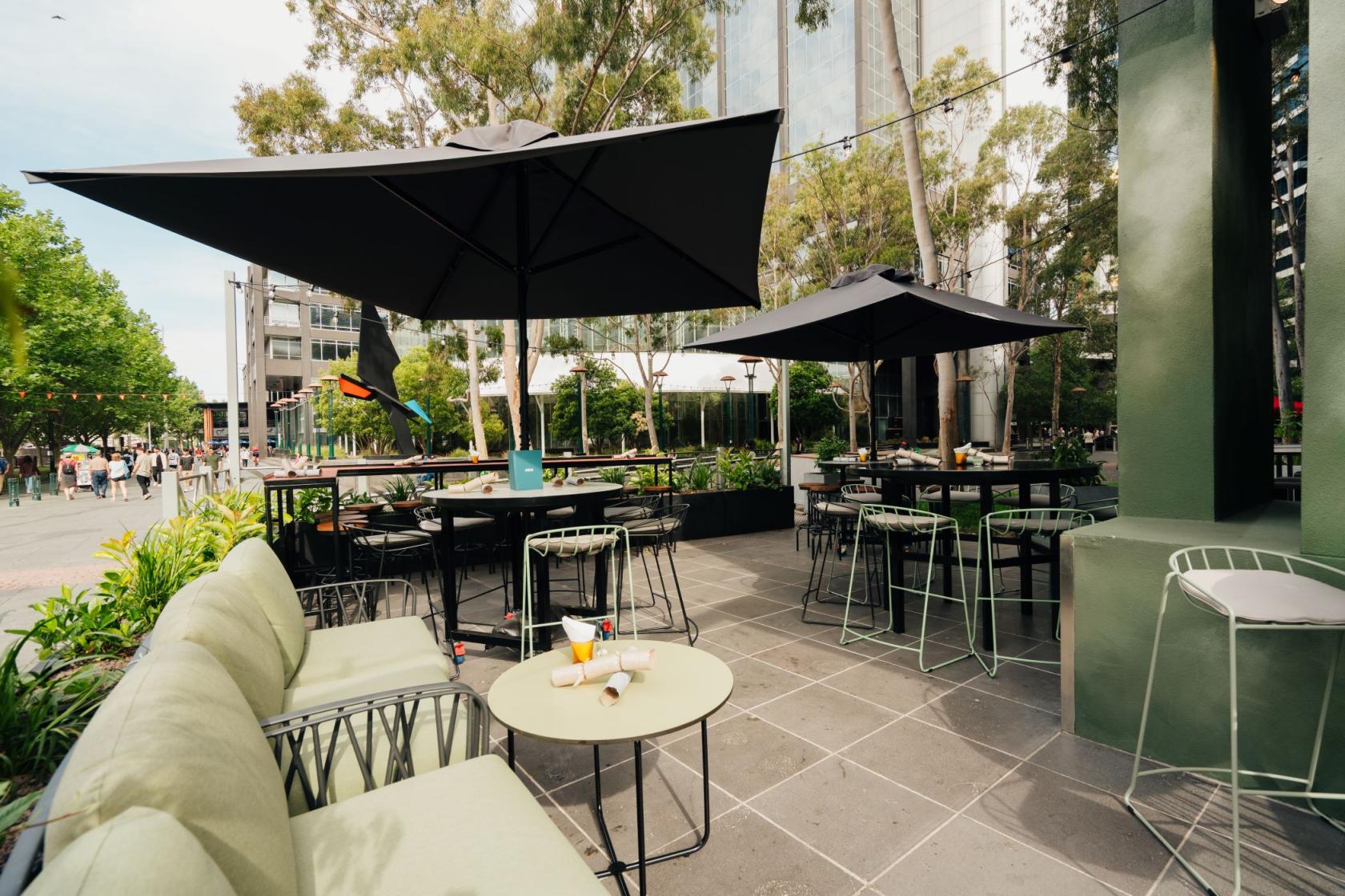 A pub terrace with outdoor seating, large umbrellas, and greenery at Ludlow Bar.