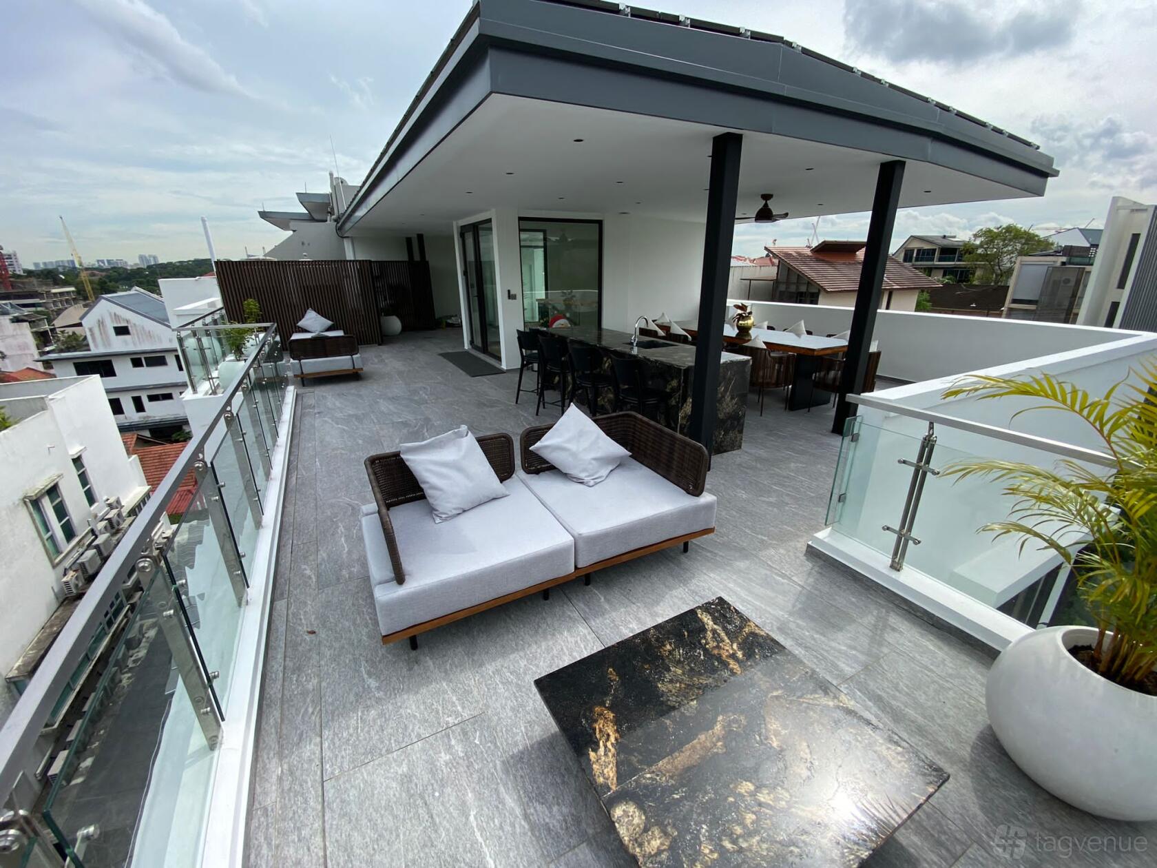 An open rooftop event venue with glass railings, marble coffee tables, and wicker sofas at ThamSoongAvenue.