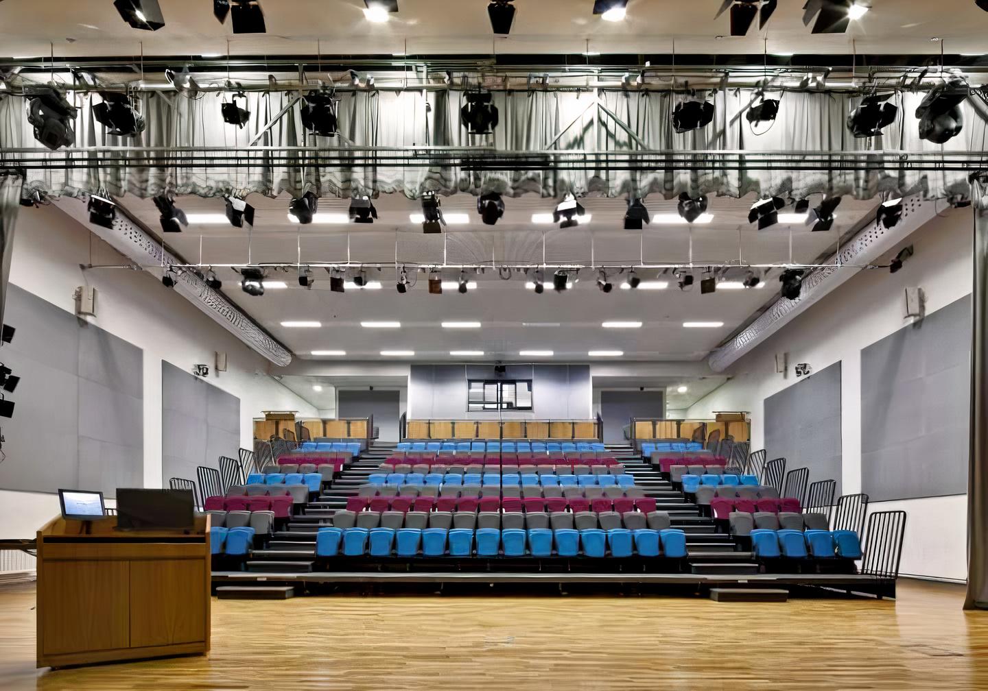 A theatre with tiered seating, overhead stage lighting, and a wooden floor at Hammersmith Academy.