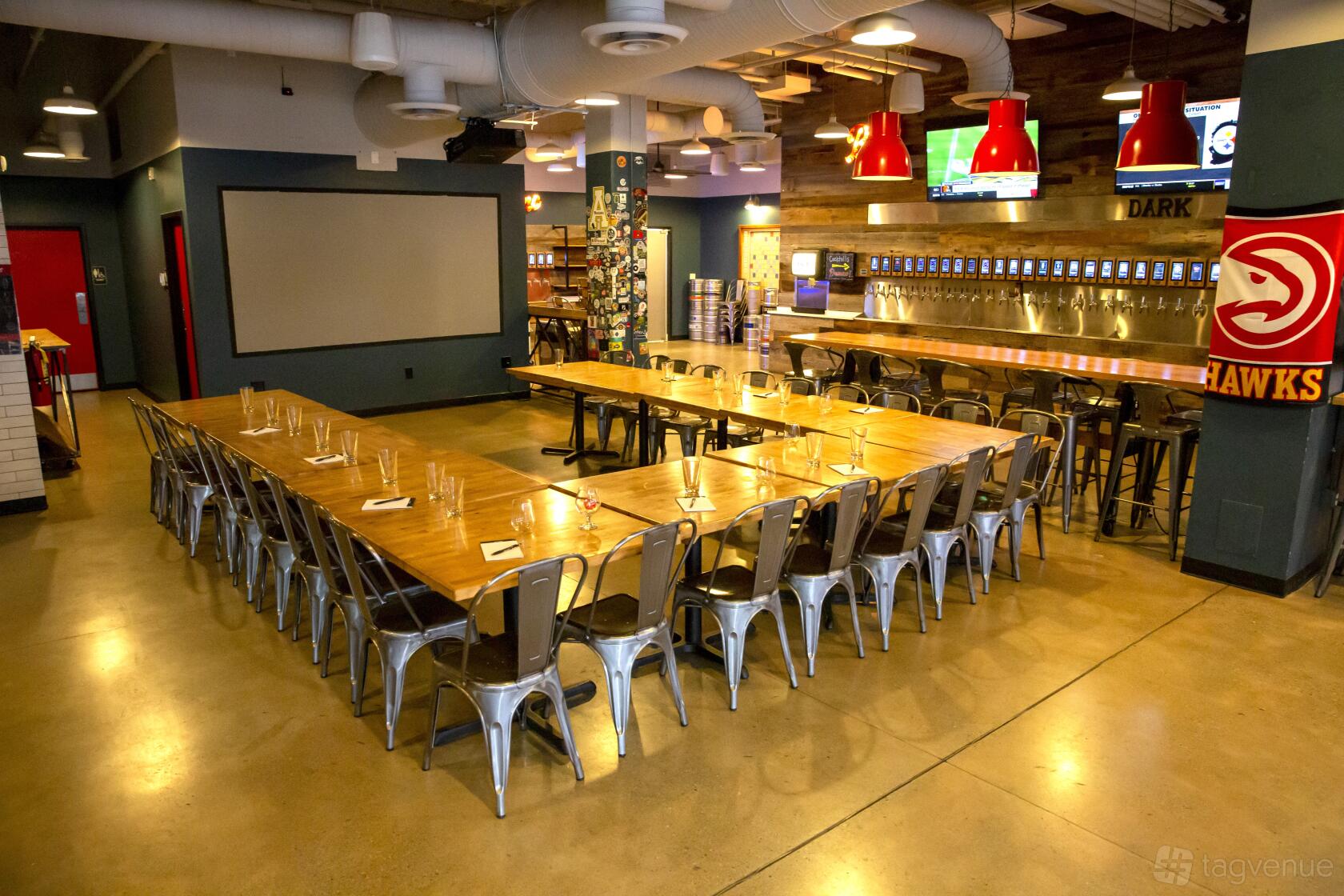 A bar with long wooden tables, metal chairs, and a self-serve tap wall at Pour Taproom Beltline.