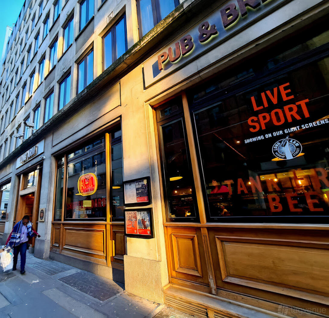 A pub with large front windows, wooden framing, and neon beer signs at Long Arm Brewery & Tap Room.