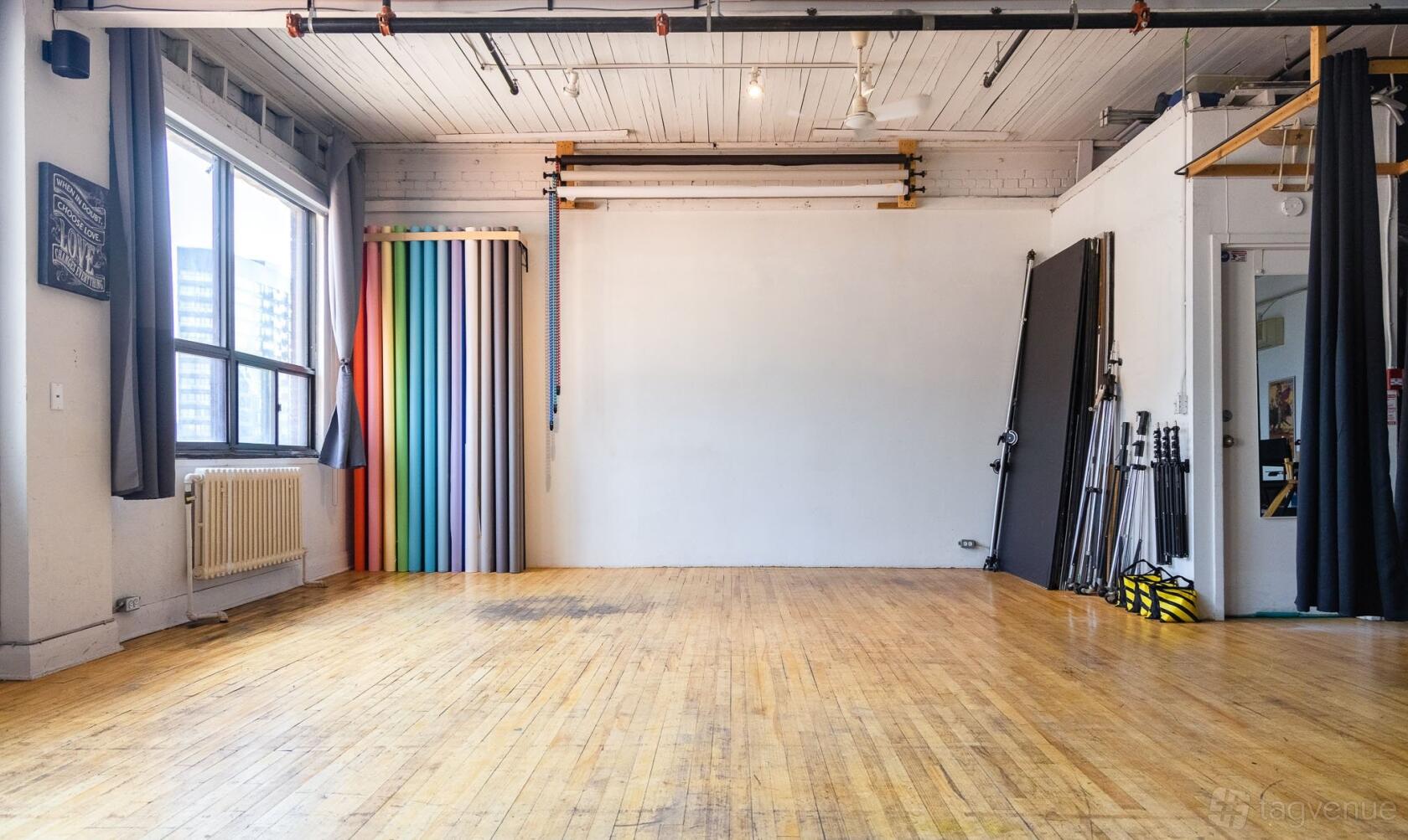 A photo studio with large windows, hardwood floors, seamless backdrops, and exposed ceiling beams at Studio 311 | Toronto Hard Loft Studio.