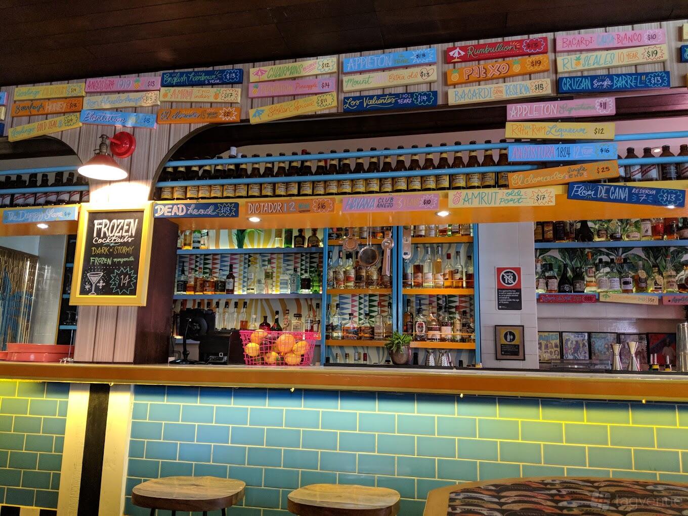 A restaurant with a colorful bar, turquoise tile backsplash, and bottles displayed on shelves at Rosie Campbell's.
