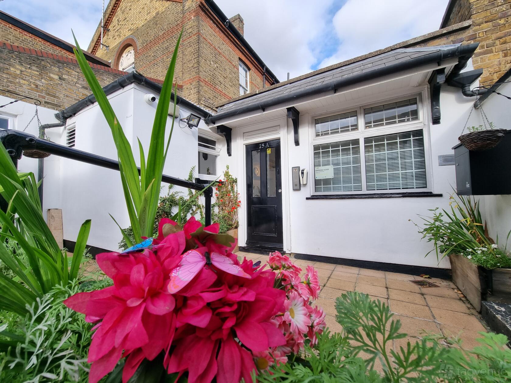 A meeting centre with a paved entrance, white exterior walls, and flower beds at Kennington Space Hire.